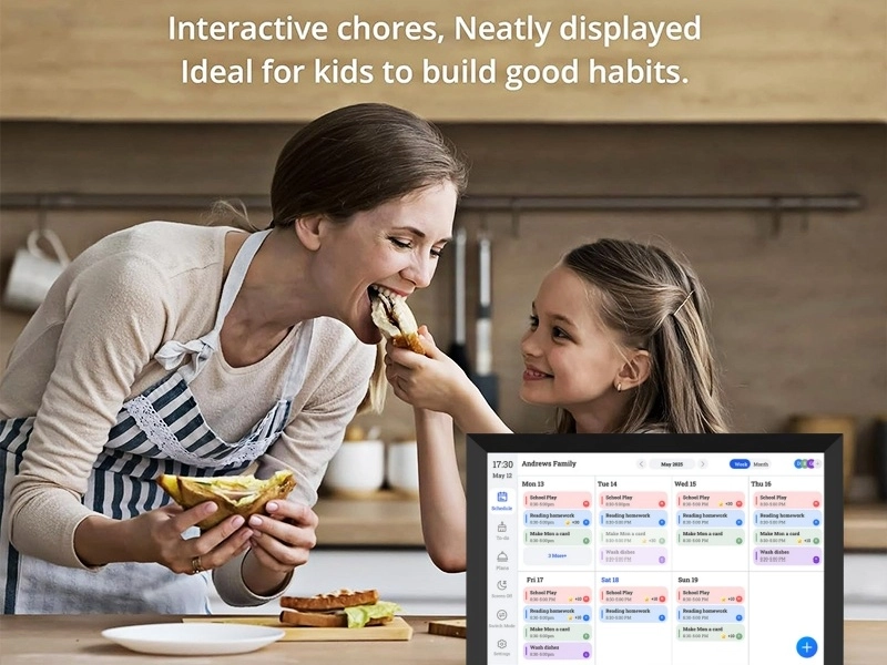 A mother and daughter smiling and sharing a sandwich in the kitchen, with a digital calendar on the counter displaying scheduled family chores