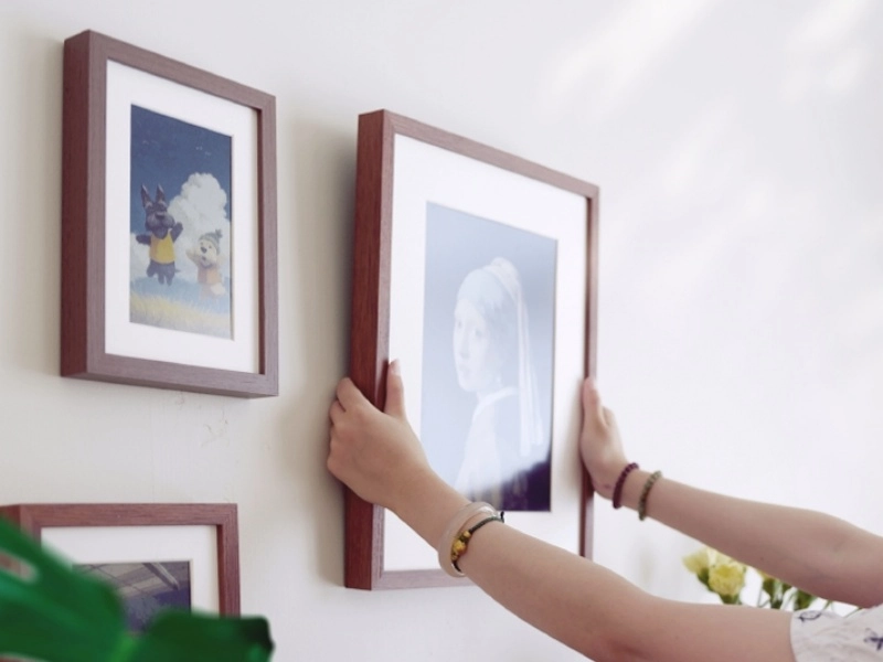 A person hanging a framed picture on a wall, adjusting the placement of the frame next to other framed artwork