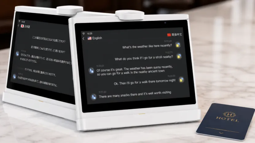 Close-up of a desktop dual-screen AI translation device displaying translated text, placed next to a hotel key card